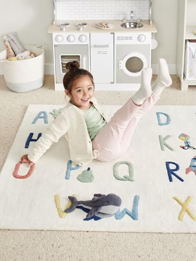 Child playing on a rug with alphabet letters in a playroom.